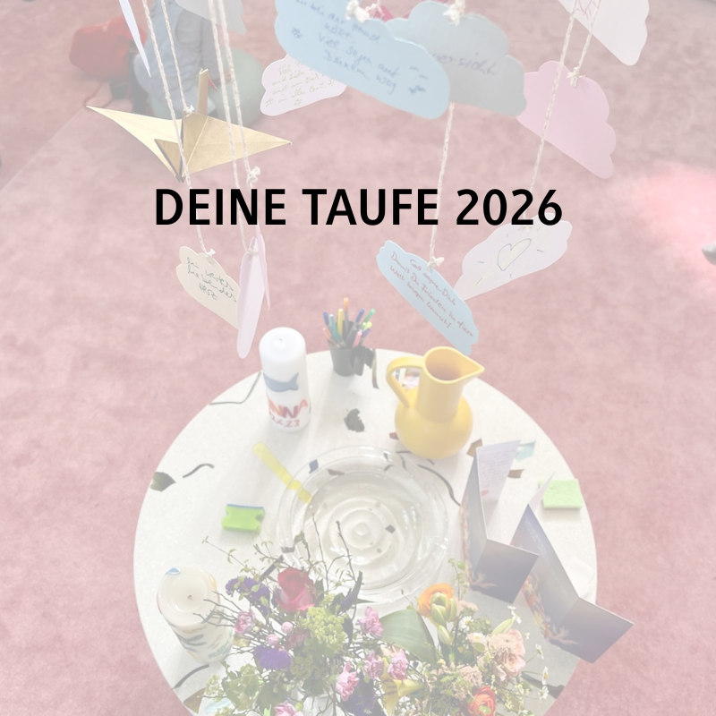 Runder Tisch mit Blumen, einem gelben Krug, Taufgegenständen und Papierwolken; "DEINE TAUFE 2026" auf rosa Hintergrund.
