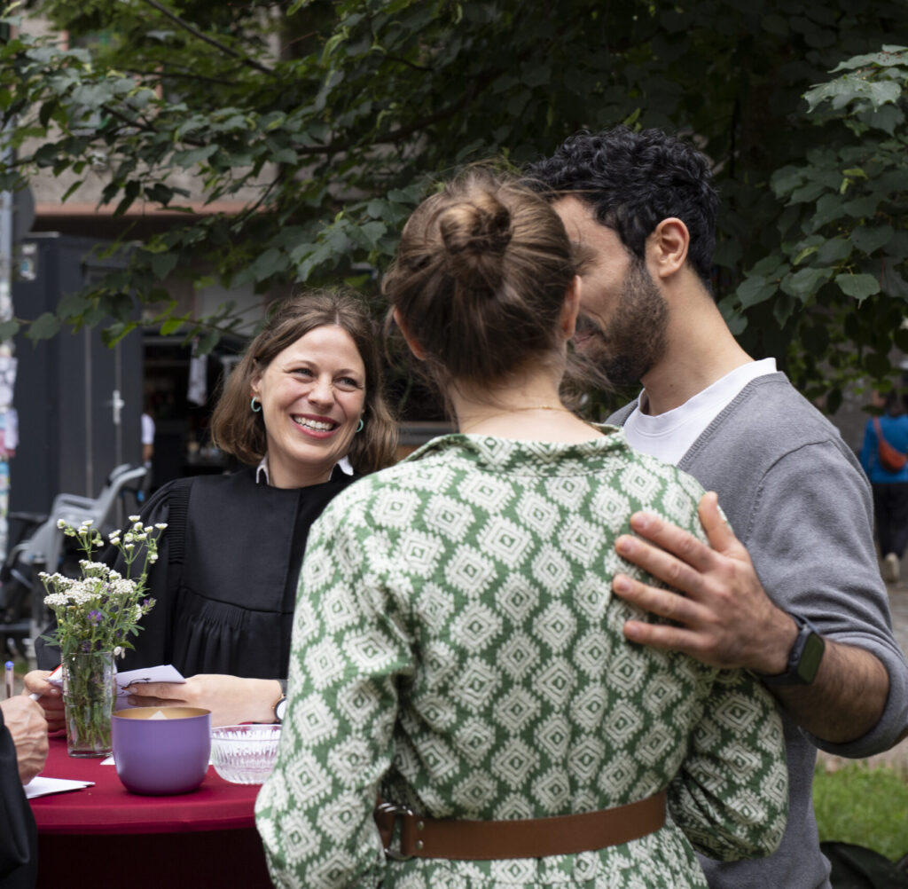Vier Erwachsene versammeln sich im Freien um einen Tisch; ein Mann in einer Robe scheint das Amt zu übernehmen.